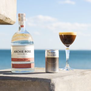 The Curatif Archie Rose Espresso Martini in a can, bottle, and glass in front of a blue ocean, one of the cocktails now available at BWS