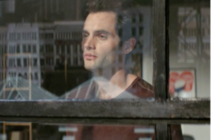 Stalker Joe Goldberg staring out a window at his next victim