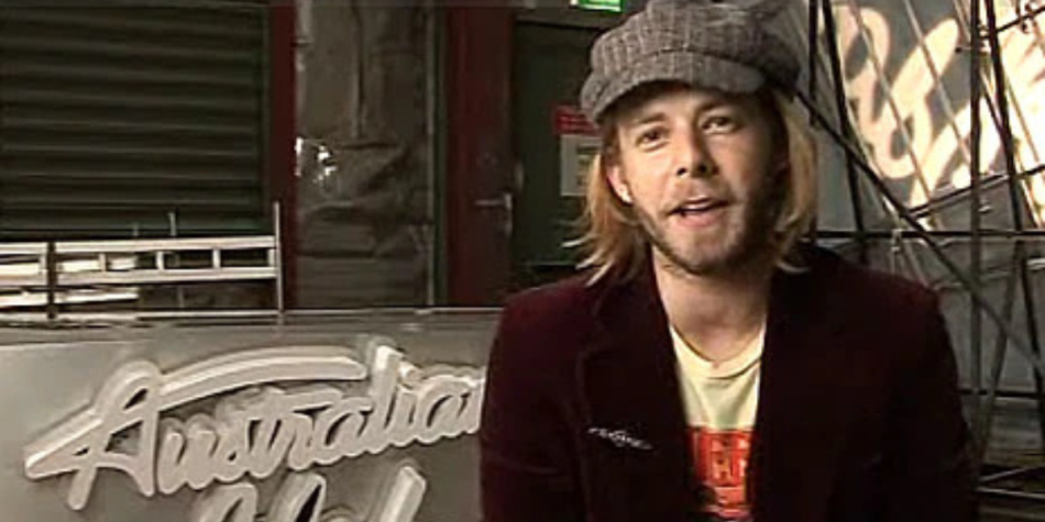 Wes Carr, winner of Australian Idol 2008, smiles during an interview segment, seated beside the show’s logo and dressed in a casual cap and jacket