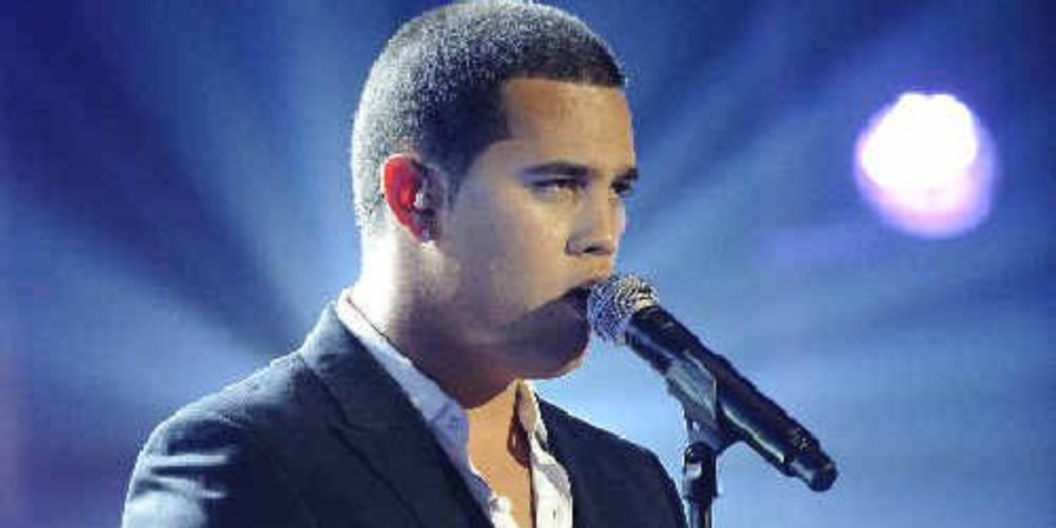 Stan Walker, winner of Australian Idol 2009, delivers an emotional performance under dramatic stage lighting, focused intently on the microphone.