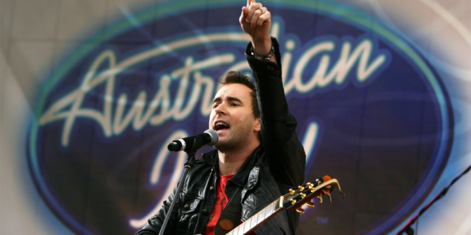 Damien Leith, winner of Australian Idol 2006, passionately performs with a guitar in hand against the iconic Australian Idol backdrop